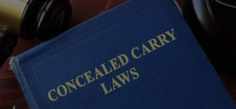 A blue book titled "Concealed Carry Laws" in gold lettering is shown close up, partially surrounded by a gavel and other objects on a wooden surface, hinting at a concealed carry law review in Missouri.