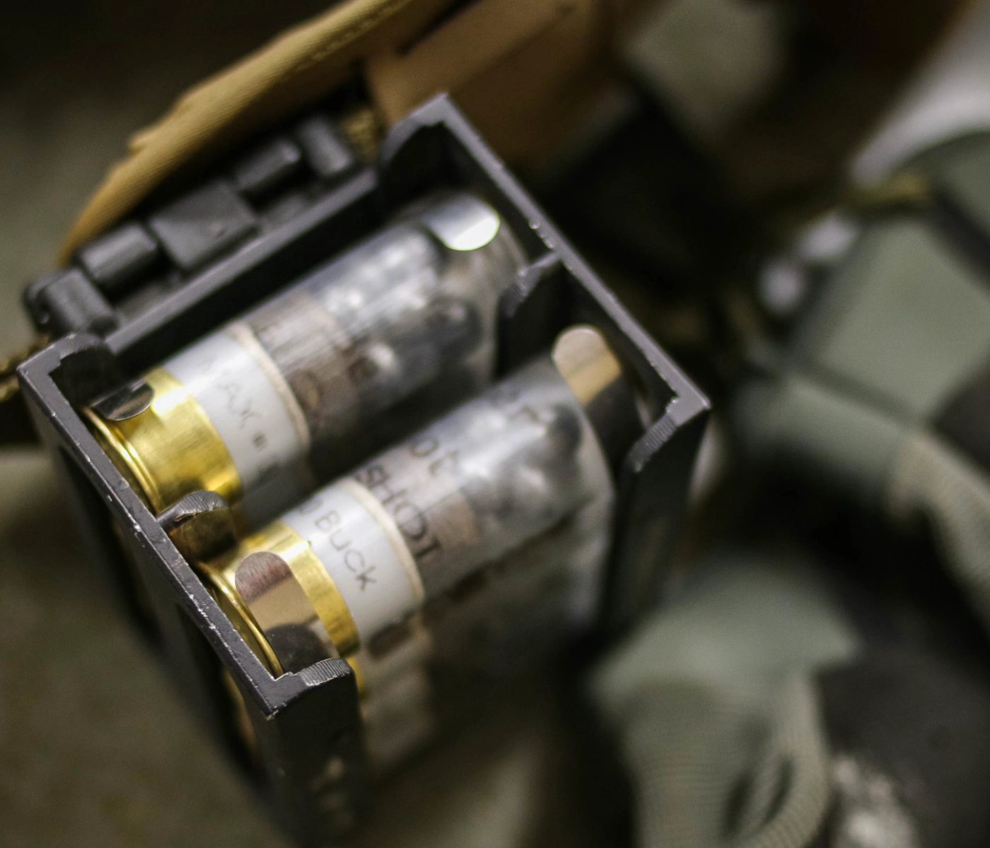 Close-up of a black ammo holder containing multiple shotgun shells labeled with text, next to a pair of gloves—ideal gear for an intermediate shotgun course in St. Louis.
