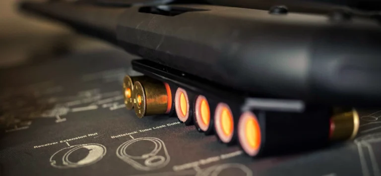 Close-up of shotgun shells in a side saddle shell holder attached to a shotgun, resting on a surface with technical firearm diagrams—ideal gear for those enrolled in an advanced shotgun course St. Louis enthusiasts trust.